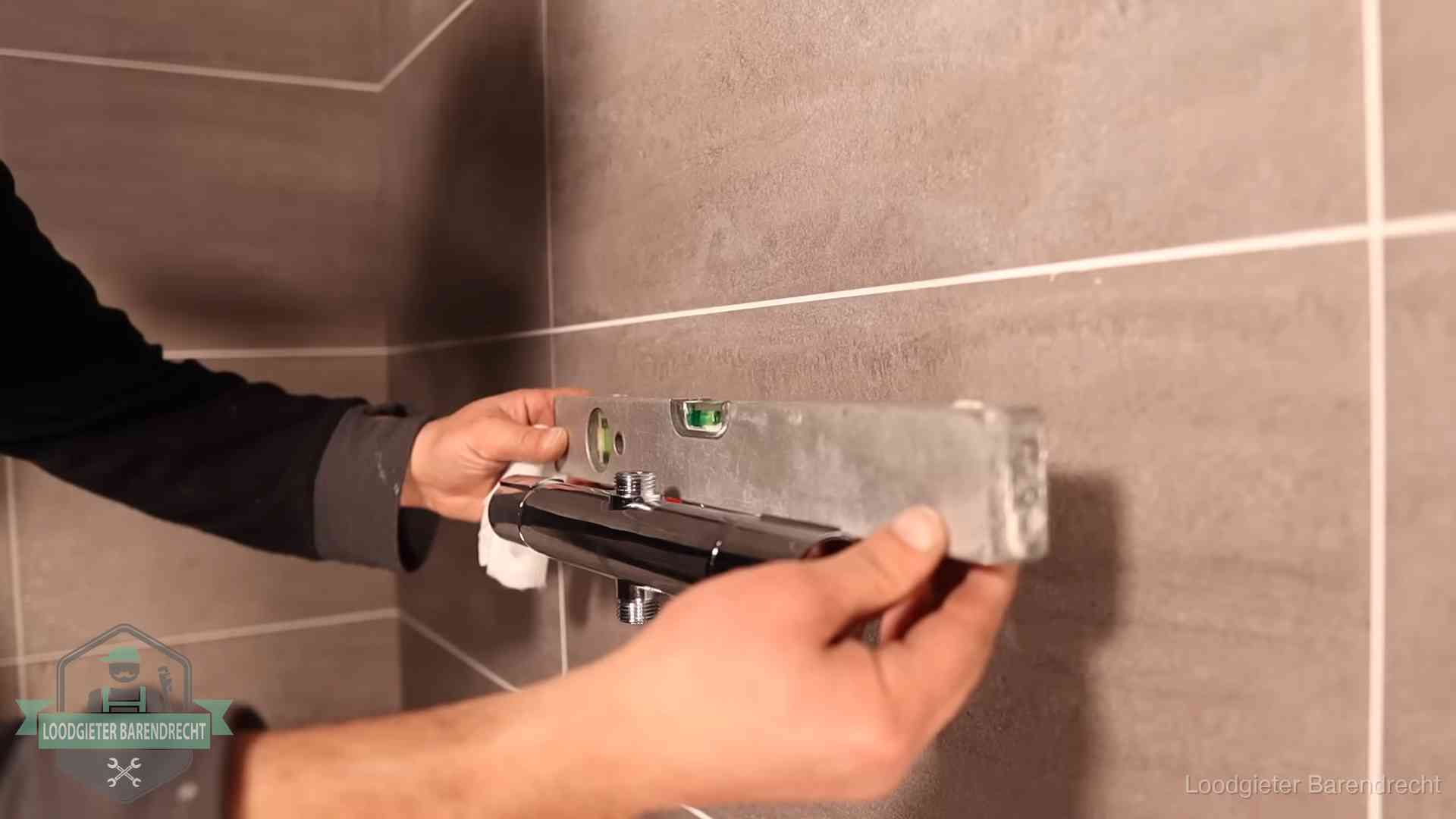 Loodgieter lijnt een douchekraan uit met een waterpas in een woning in Barendrecht