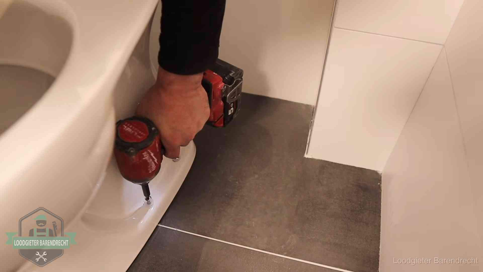 Kosten wc ontstoppen in Barendrecht Loodgieter zet de voet van een wc-pot vast op de tegelvloer in Barendrecht